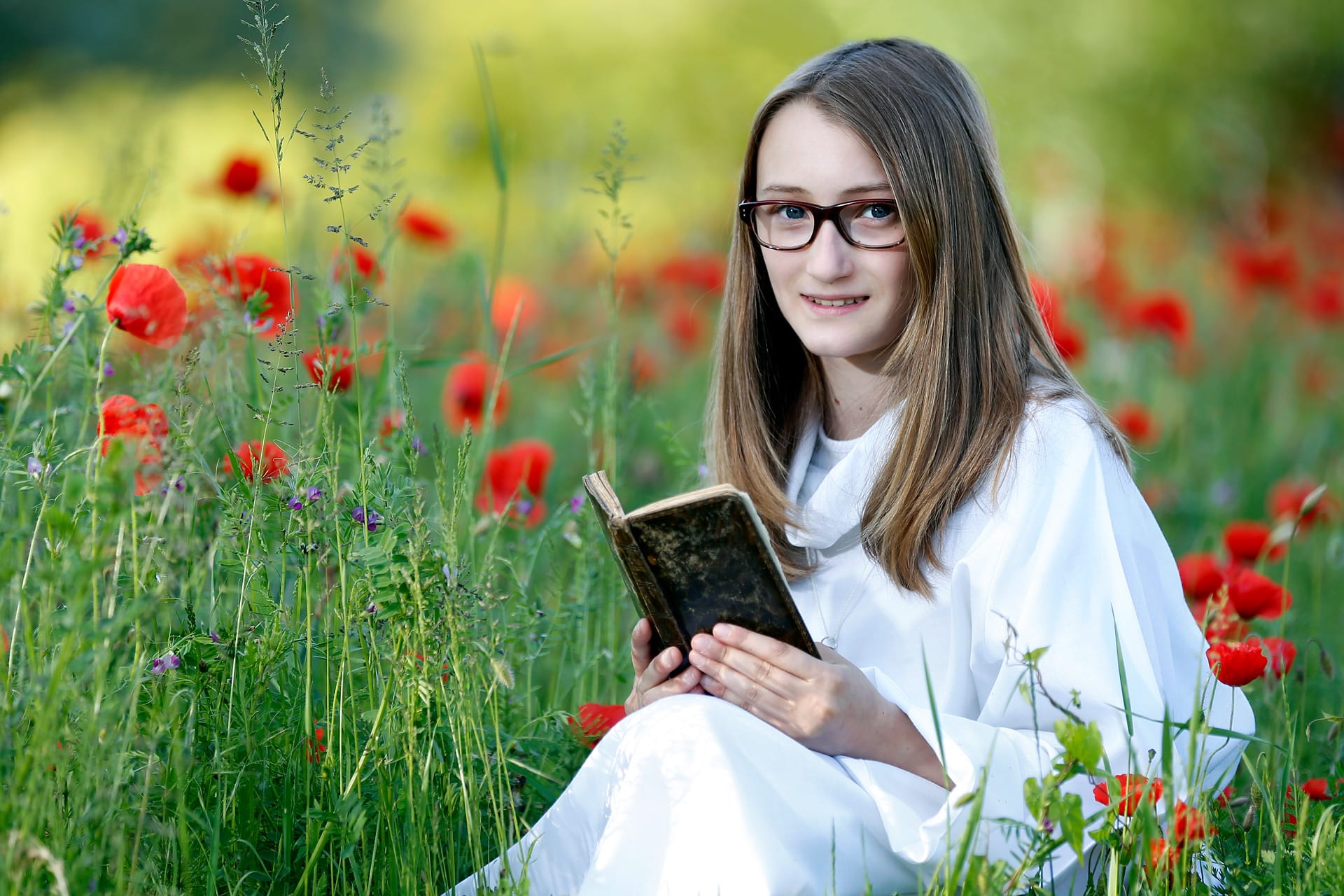 Jeune fille assise dans un champ de coquelicots avec une Bible par Franck Chazelet